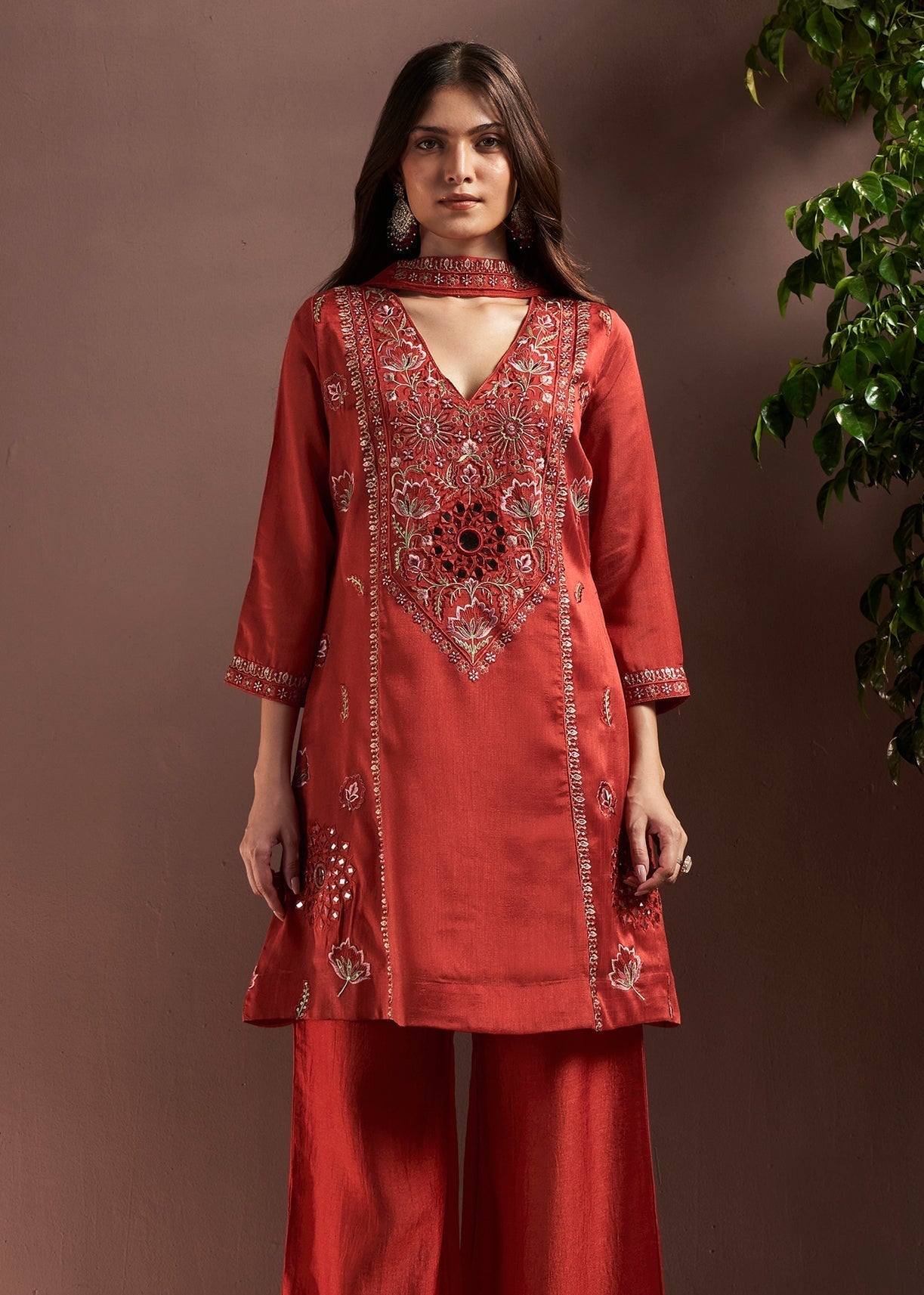 Woman wearing a red embroidered outfit against a brown background