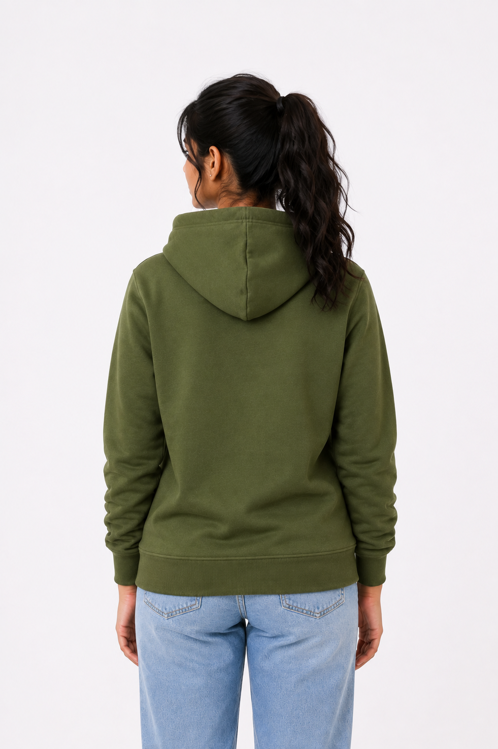 A woman viewed from behind wearing an olive green pullover hoodie and light blue jeans against a plain white studio background.