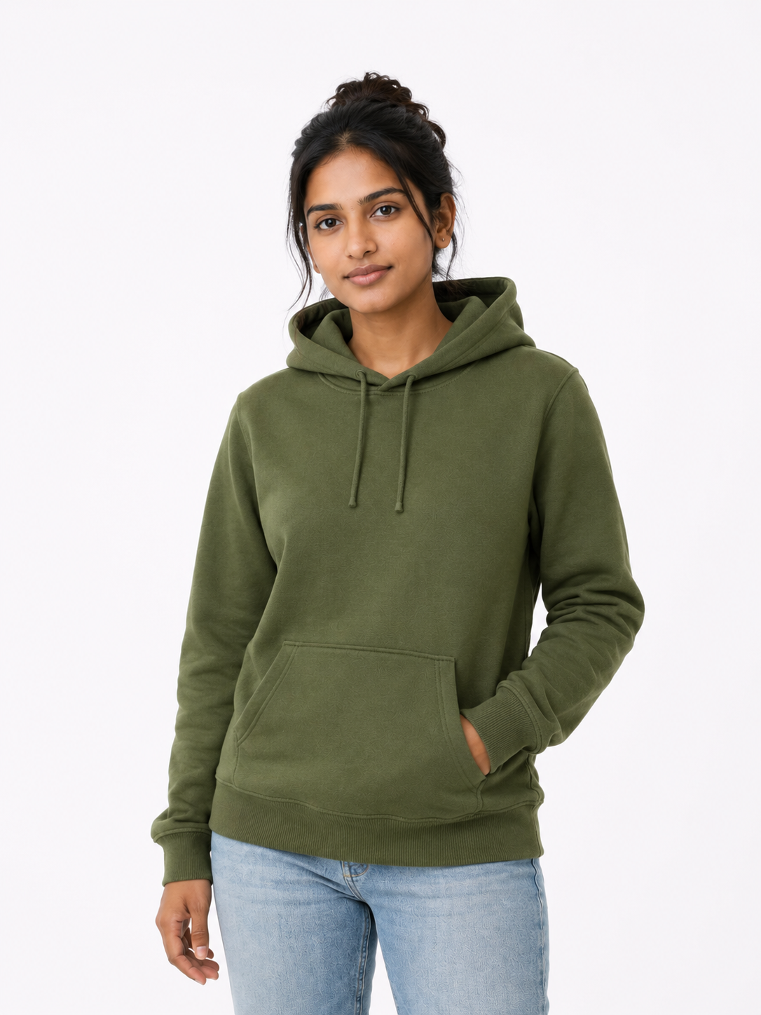 A woman wearing an olive green pullover hoodie with drawstrings and a front kangaroo pocket, paired with light blue jeans, photographed against a plain light gray studio background.
