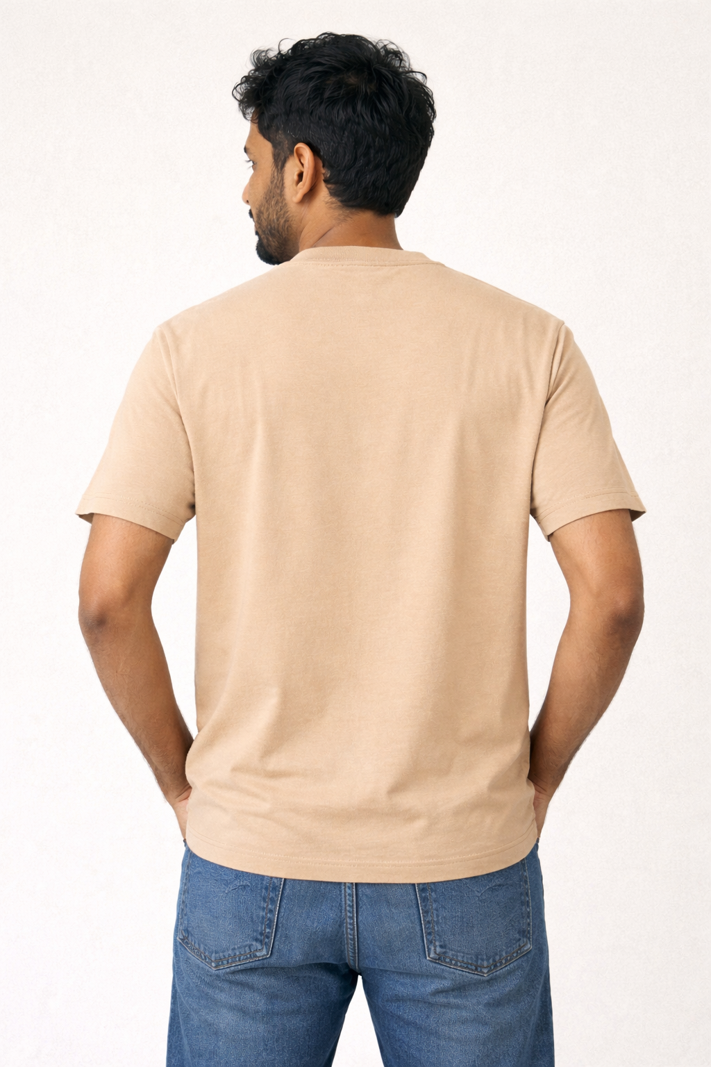Man wearing a beige t-shirt and blue jeans on a white background