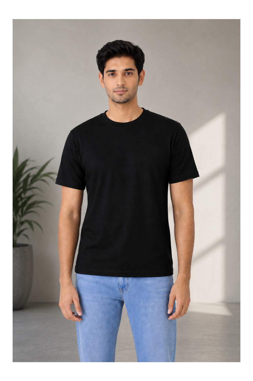 Man wearing a black t-shirt and light blue jeans standing against a neutral background