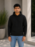 Man wearing a black hoodie and blue jeans standing outdoors.