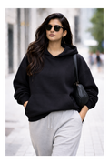 Woman wearing a black hoodie and gray pants walking on a street.