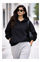 Woman wearing a black hoodie and gray pants walking on a street.