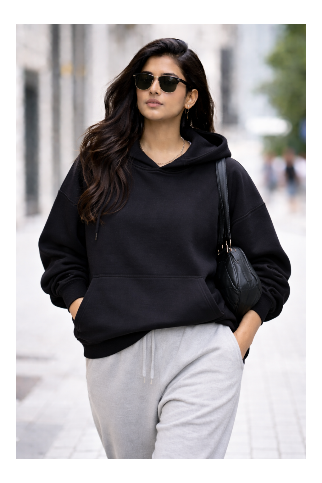 Woman wearing a black hoodie and gray pants walking on a street.