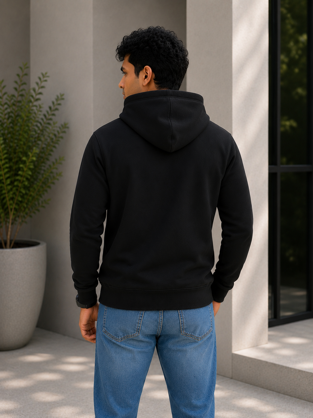 Person wearing a black hoodie and blue jeans standing outdoors.