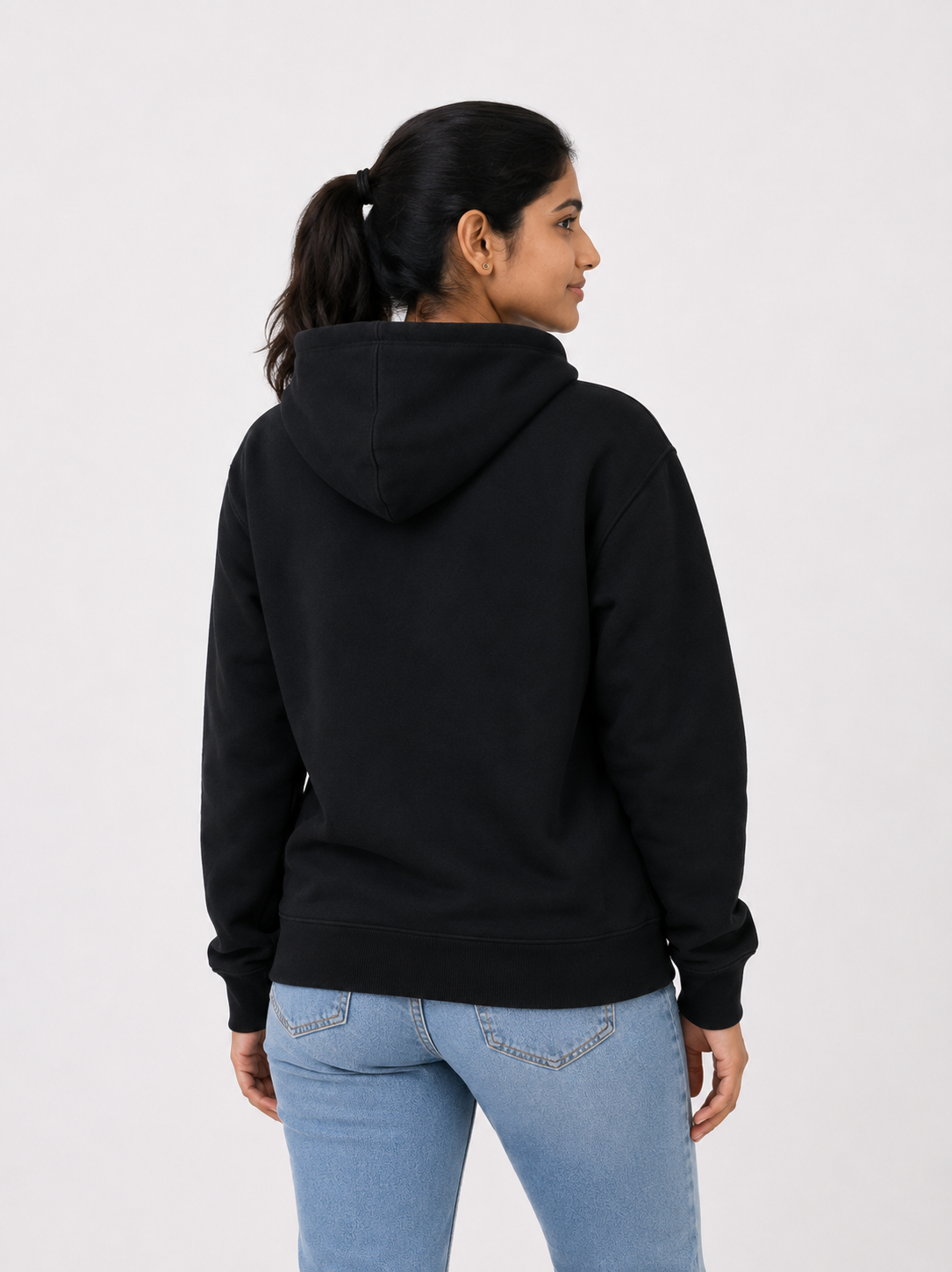A woman shown from the back wearing a black pullover hoodie and light blue jeans, photographed against a plain light gray studio background.
