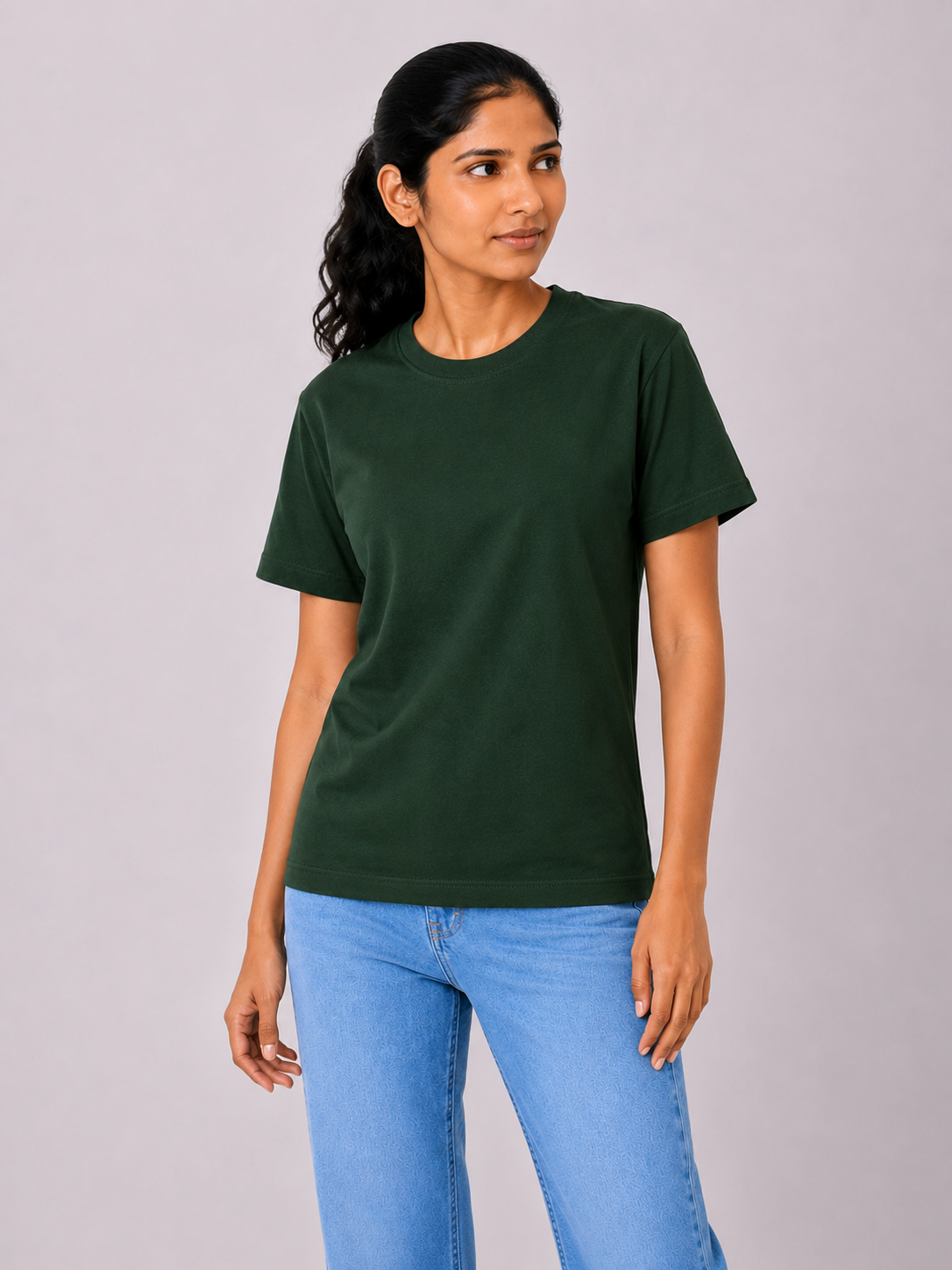 Woman wearing a dark green t-shirt and blue jeans on a gray background