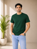 Man wearing a green t-shirt and light blue jeans standing indoors with a plant in the background