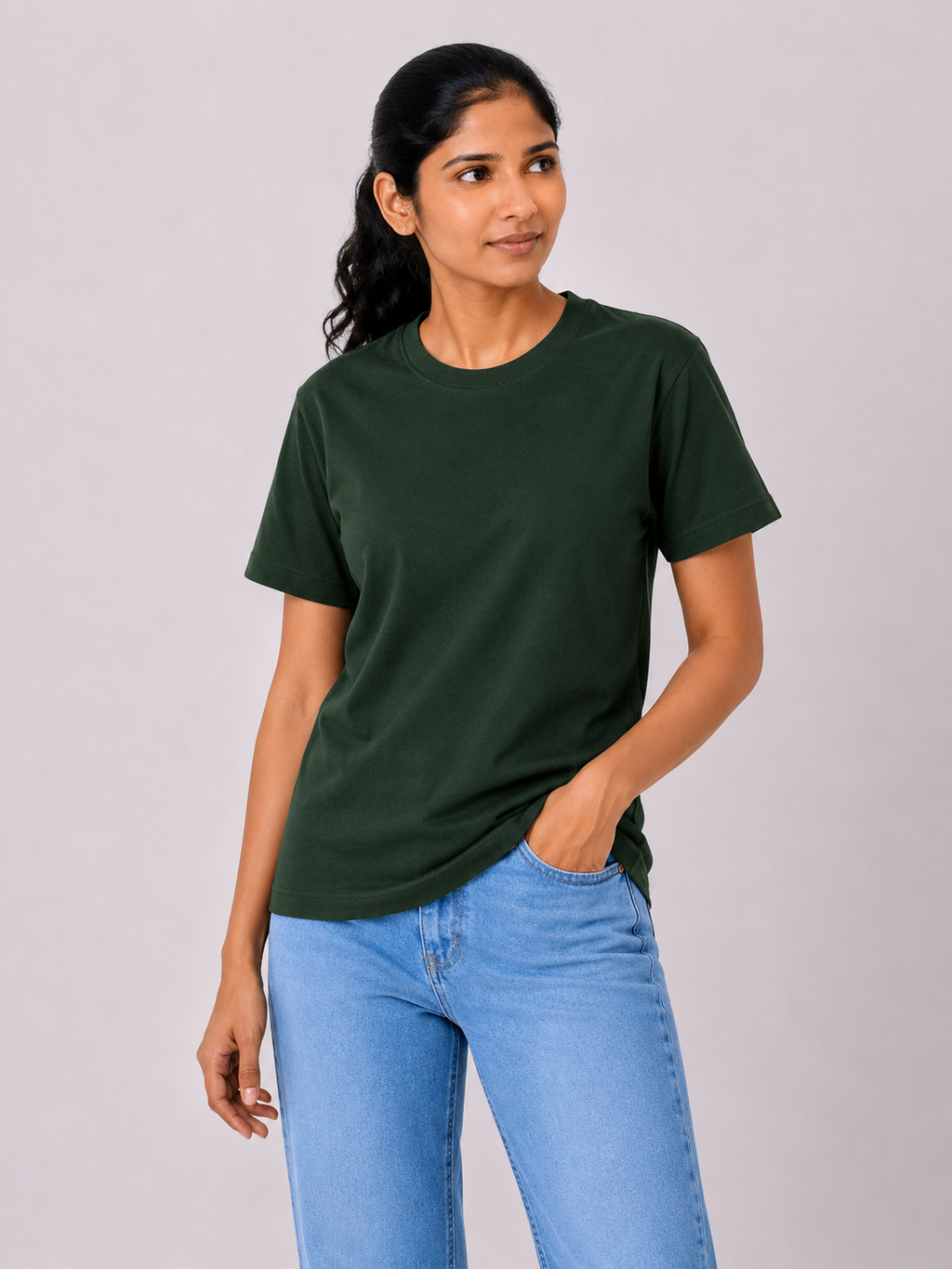 Woman wearing a dark green t-shirt and light blue jeans against a plain background