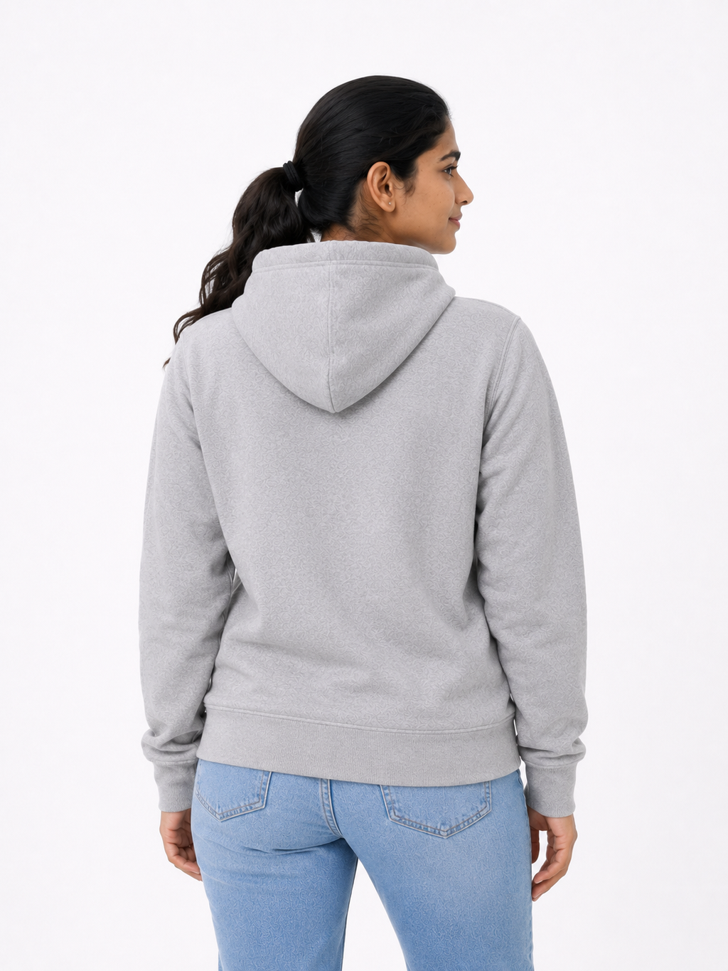 A woman shown from the back wearing a light gray heathered zip-up hoodie and light blue jeans, photographed against a clean white studio background.