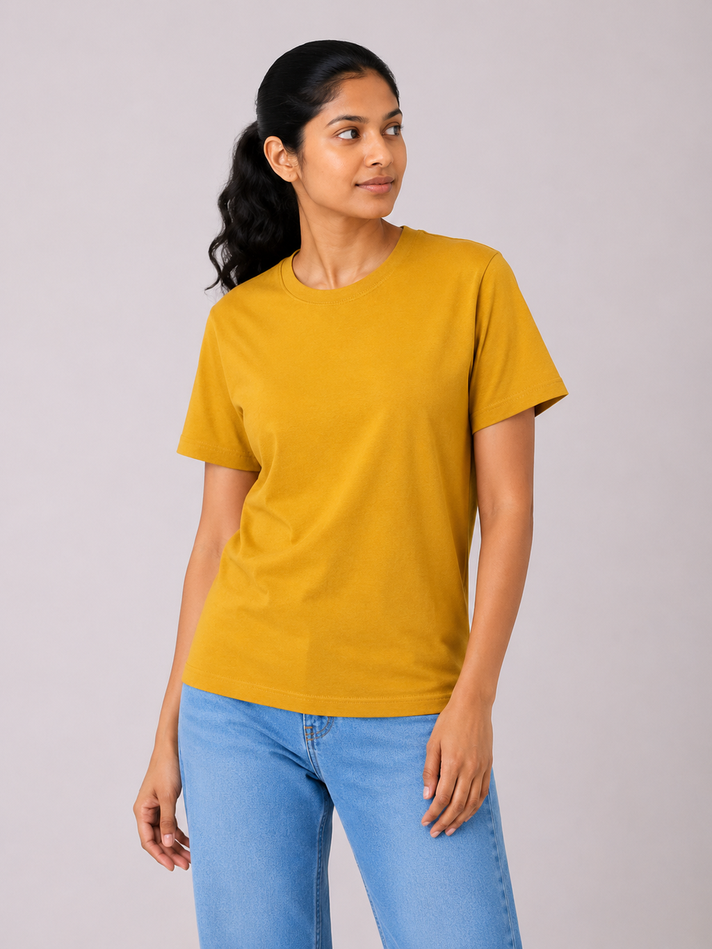Woman wearing a mustard yellow t-shirt and blue jeans against a plain background