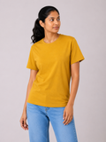Woman wearing a mustard yellow t-shirt and blue jeans against a plain background