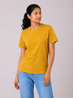Woman wearing a mustard yellow t-shirt and blue jeans against a plain background