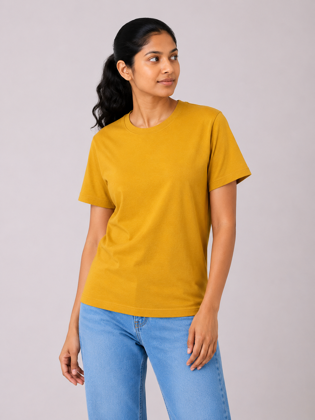 Woman wearing a mustard yellow t-shirt and blue jeans against a plain background