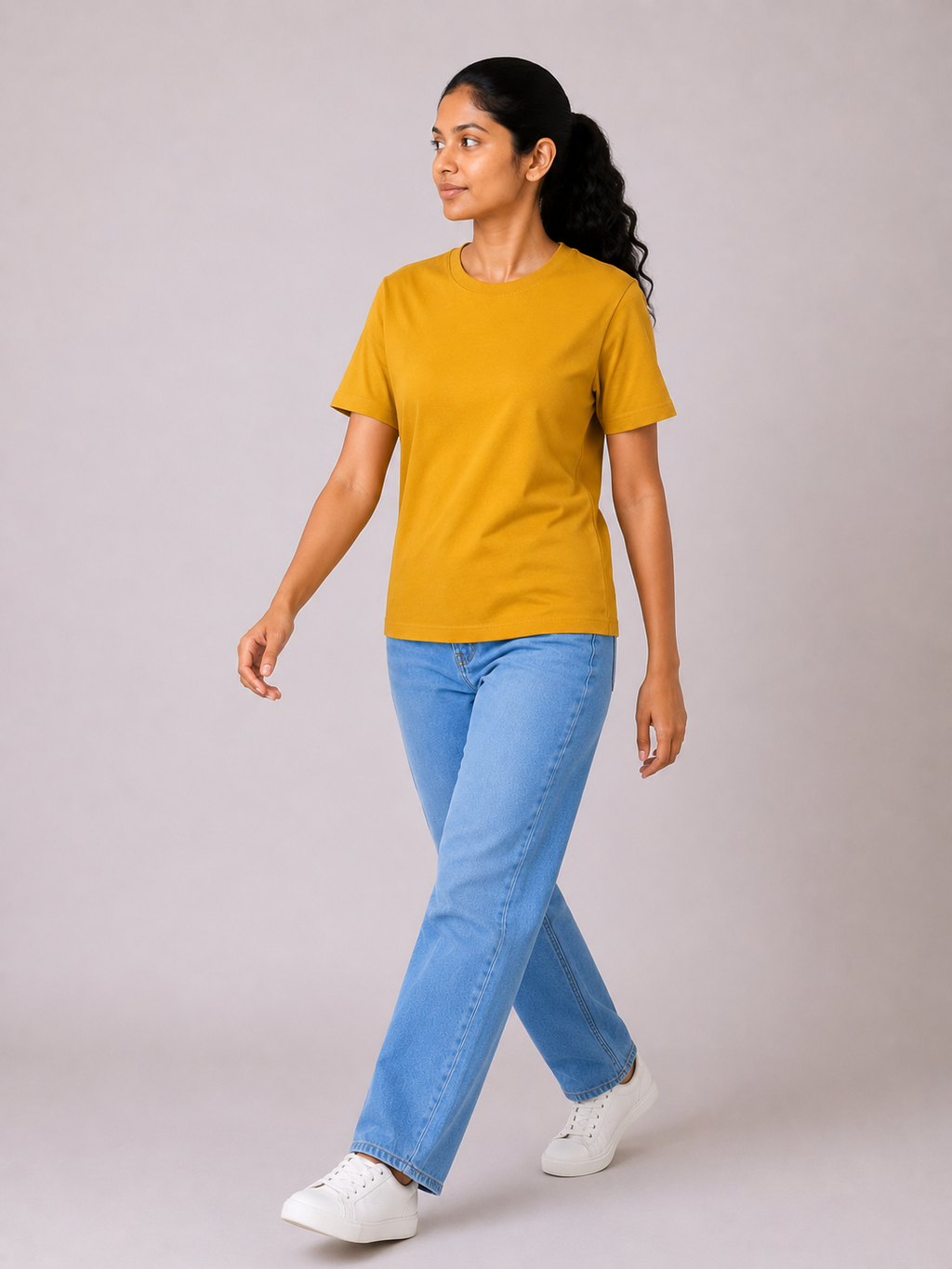 Woman wearing a mustard yellow t-shirt and blue jeans on a plain background
