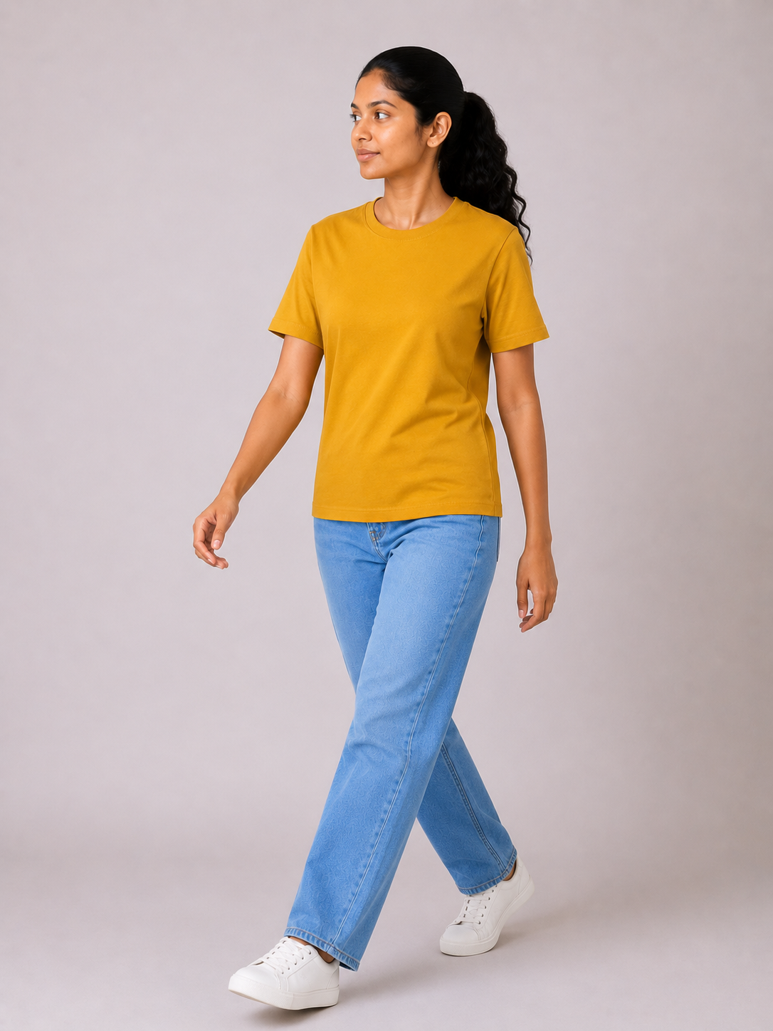 Woman wearing a mustard yellow t-shirt and blue jeans on a plain background