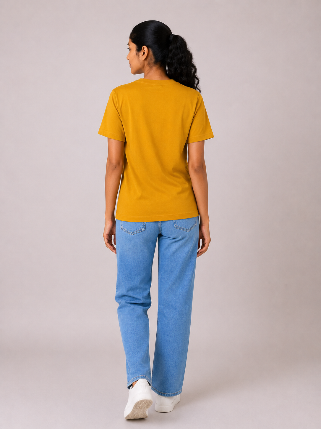 Person wearing a mustard yellow t-shirt and blue jeans on a plain background