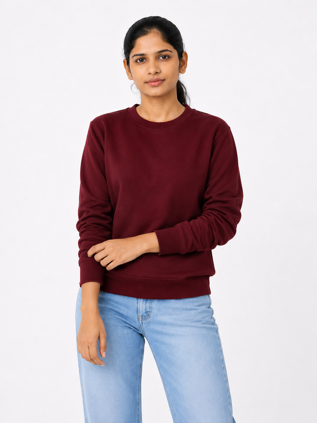 Woman wearing a maroon sweater and light blue jeans on a white background
