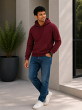 Man wearing a maroon hoodie and blue jeans standing outdoors near a building.