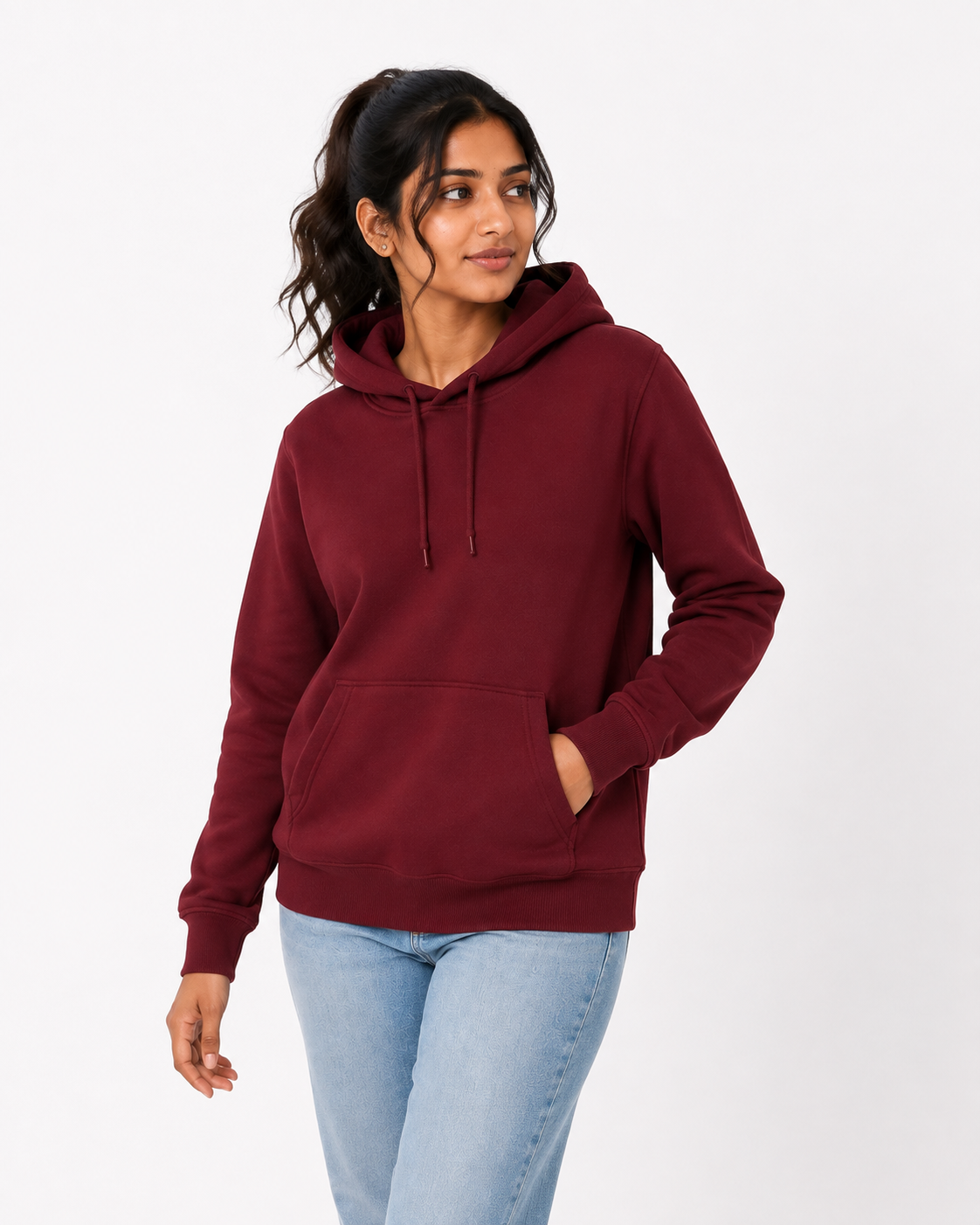 A woman wearing a maroon pullover hoodie with a drawstring hood and kangaroo pocket, paired with light blue jeans, standing against a plain white studio background.