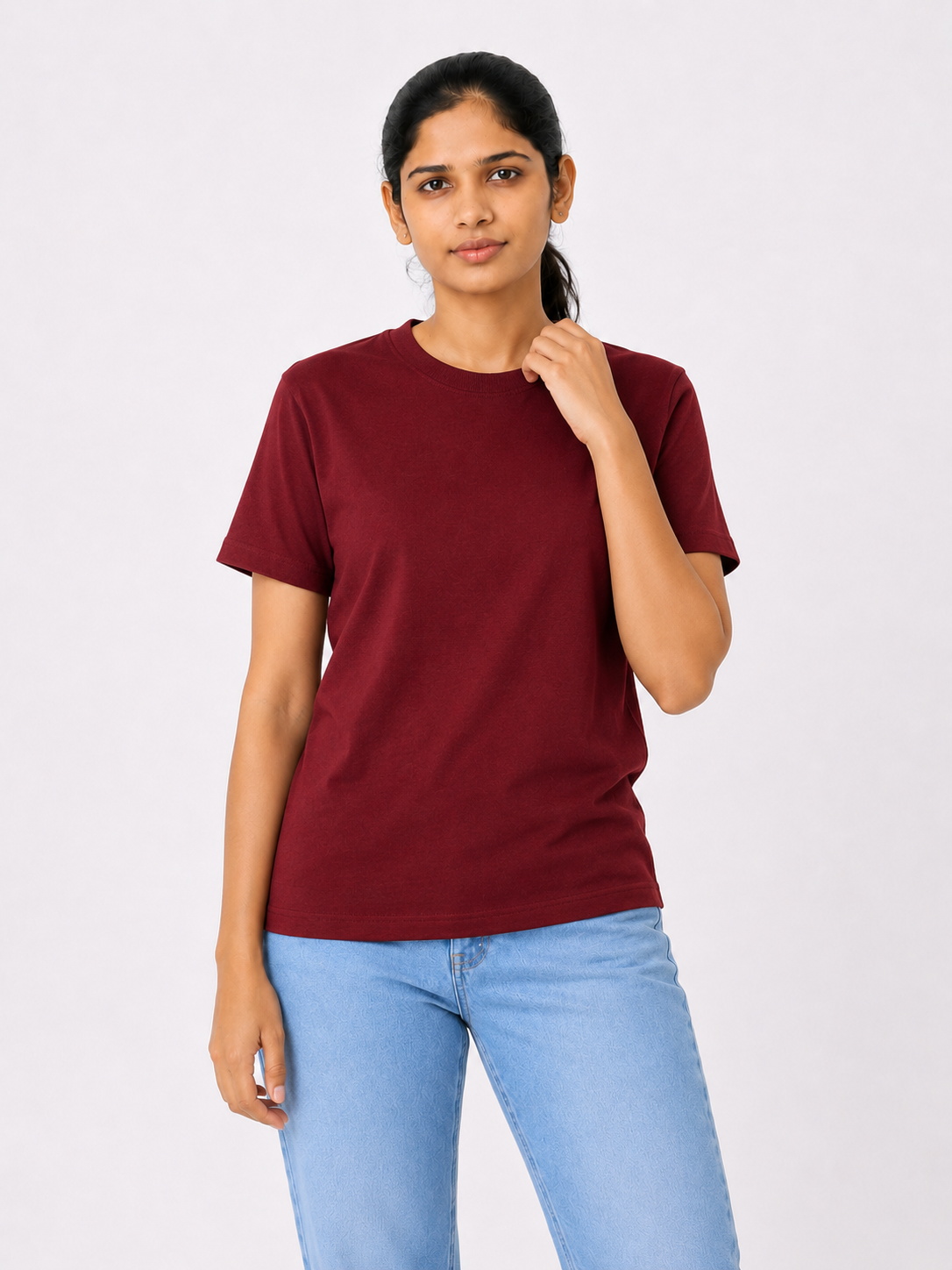Woman wearing a maroon t-shirt and light blue jeans on a white background