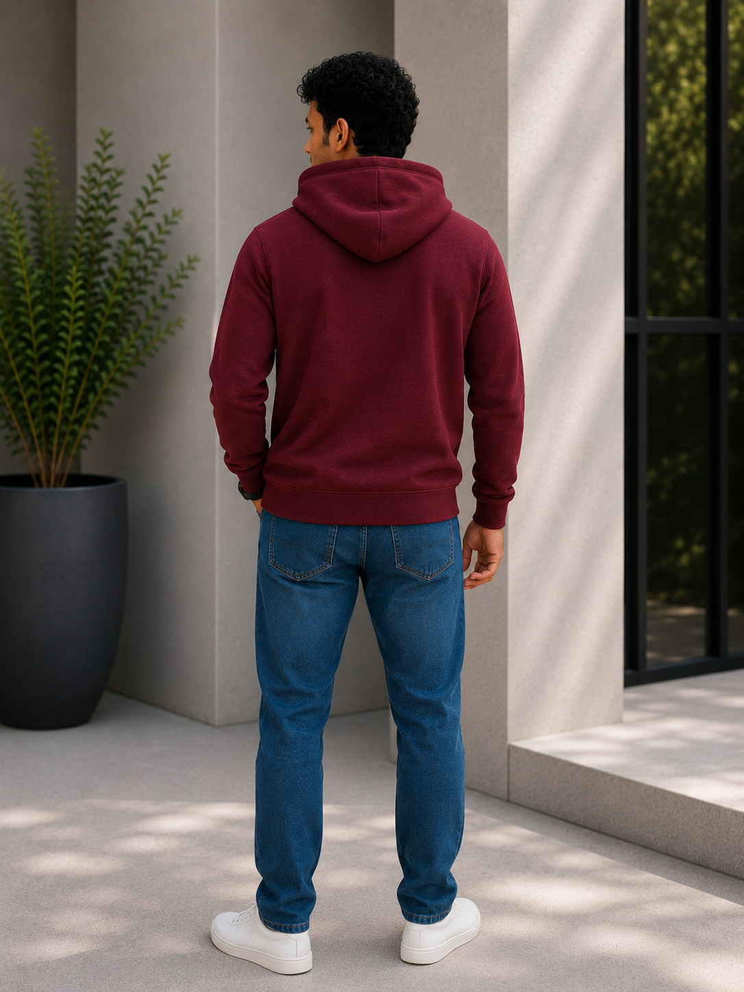 Person wearing a maroon hoodie and blue jeans standing outdoors.