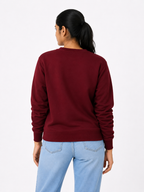 Person wearing a maroon sweatshirt and light blue jeans on a white background