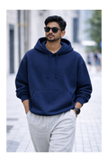 Man wearing a navy blue hoodie and light gray pants on a blurred city street background