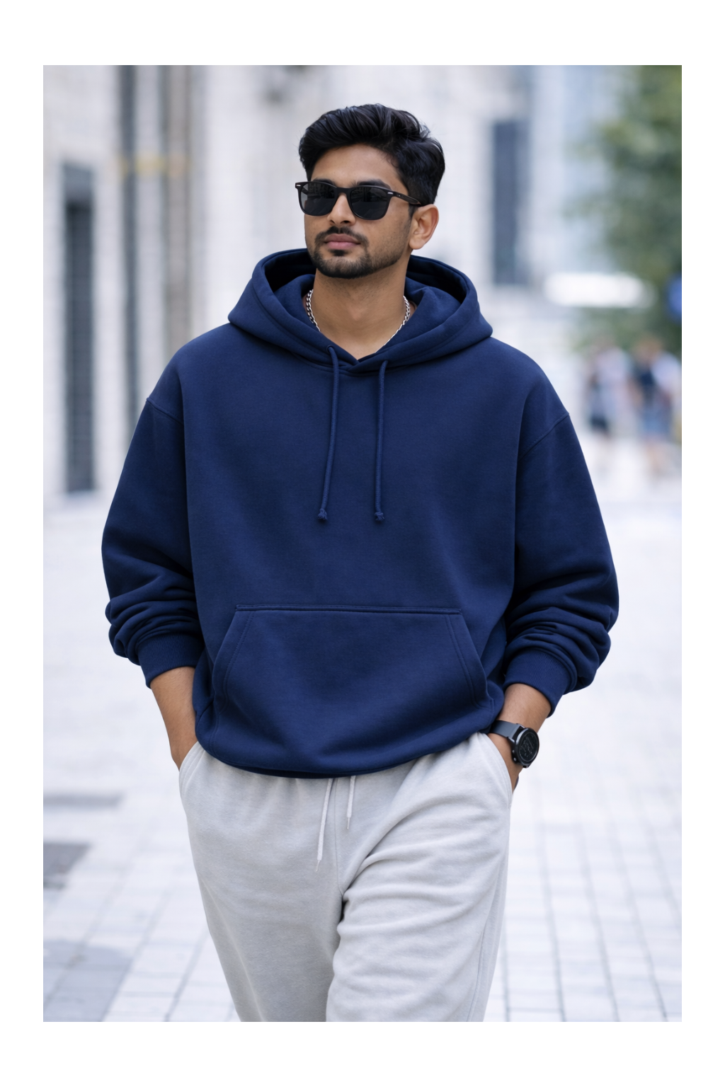 Man wearing a navy blue hoodie and light gray pants on a blurred city street background