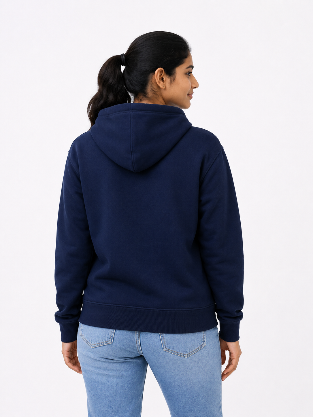 A woman shown from the back wearing a navy blue pullover hoodie and light blue jeans against a plain white studio background.