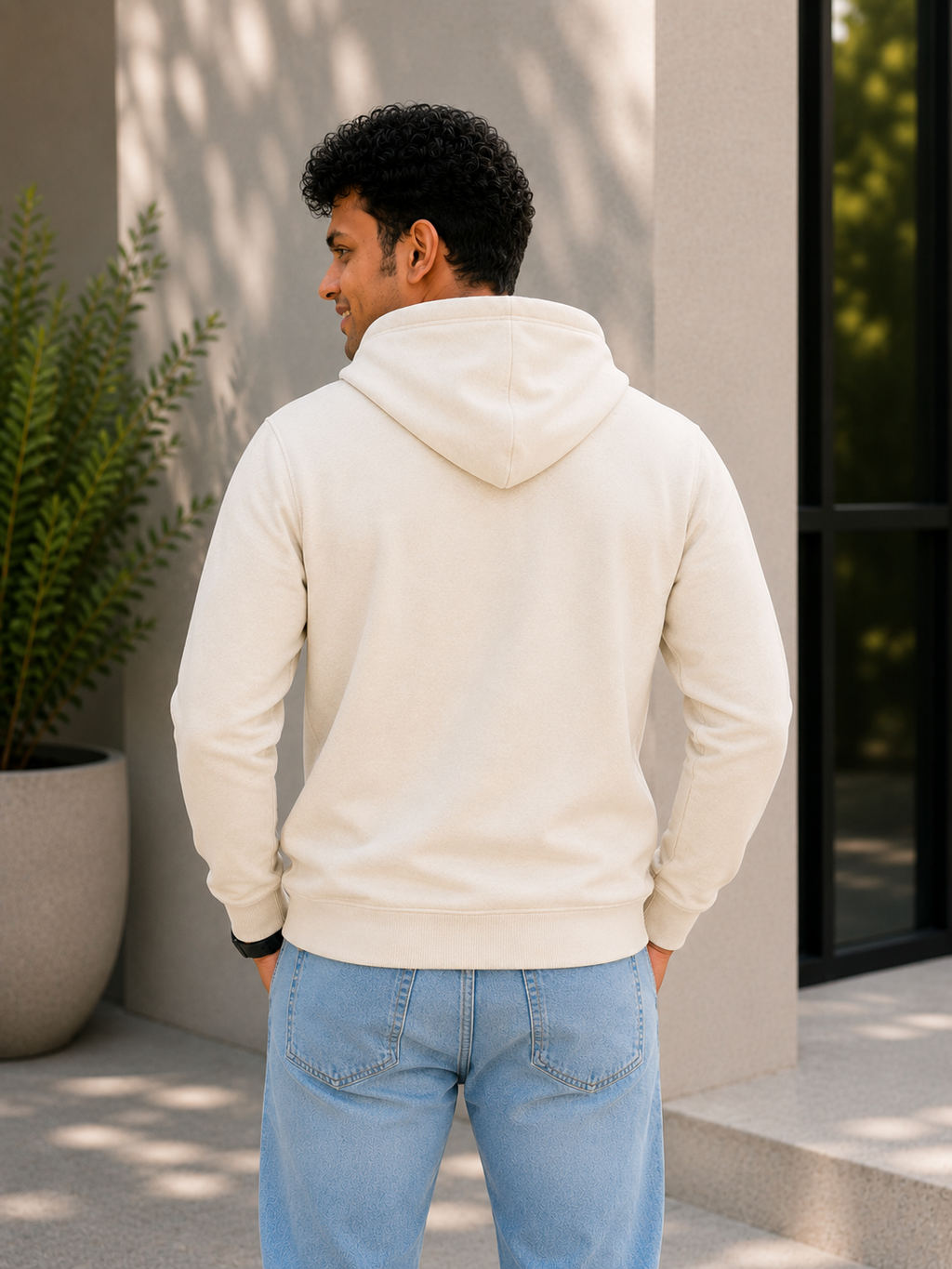 Man wearing a beige hoodie and light blue jeans standing outdoors.