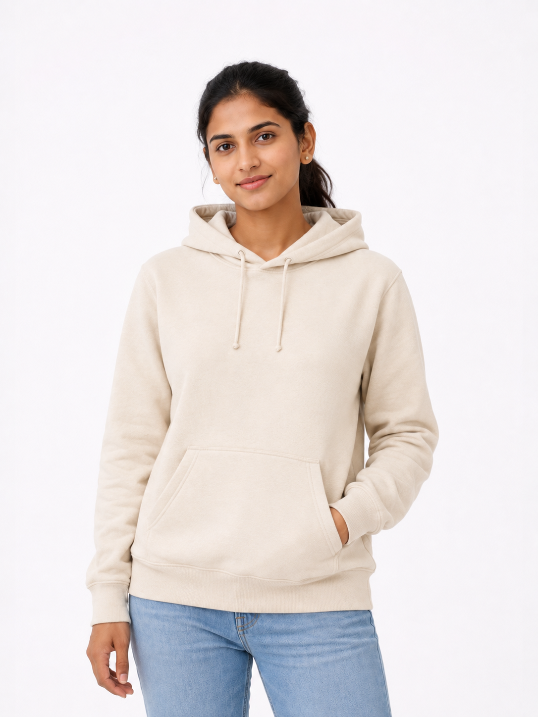 A woman wearing a light beige pullover hoodie with drawstrings and a front kangaroo pocket, paired with light blue jeans, against a plain white studio background.