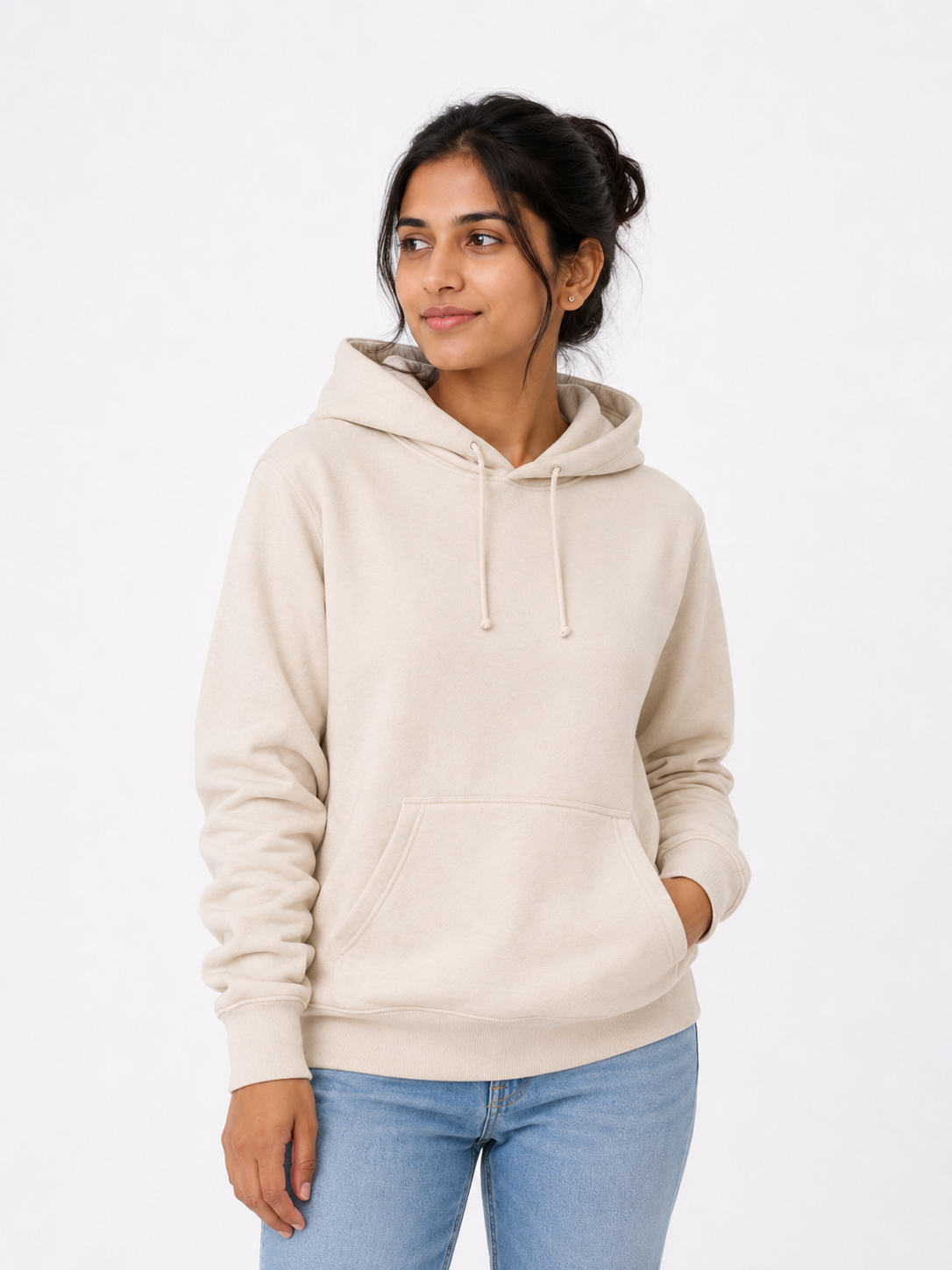 A woman wearing a light beige pullover hoodie with drawstrings and a front kangaroo pocket, paired with light blue jeans, photographed against a plain white studio background.