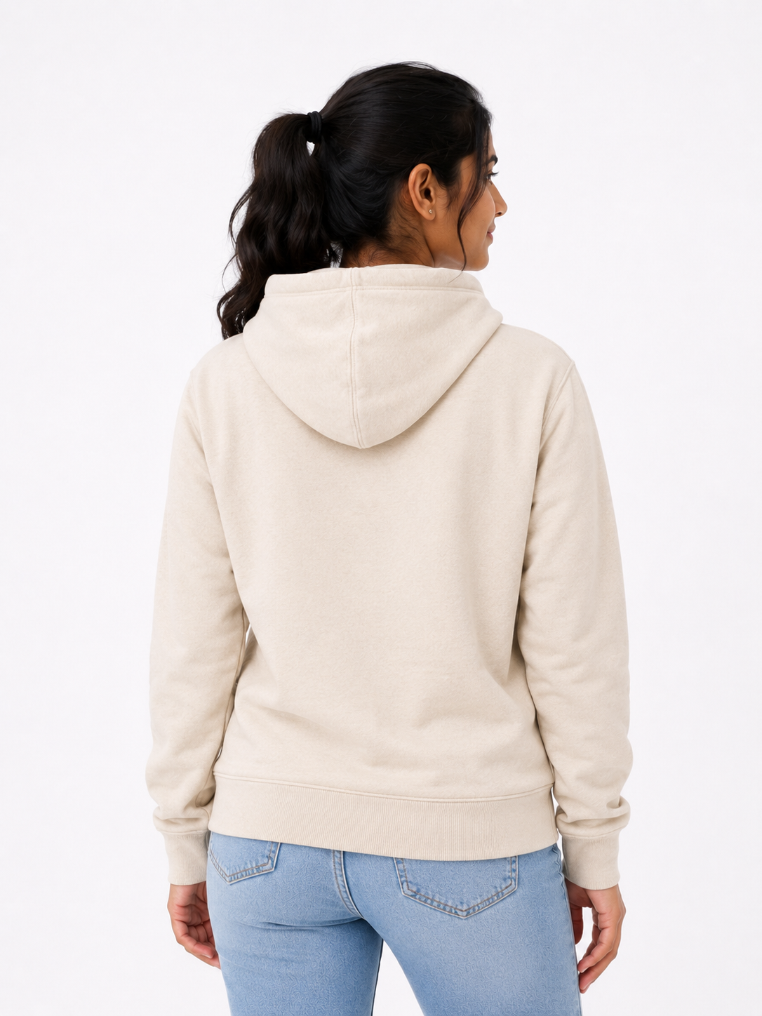A woman shown from the back wearing a light beige hooded sweatshirt and light blue jeans against a plain white studio background.