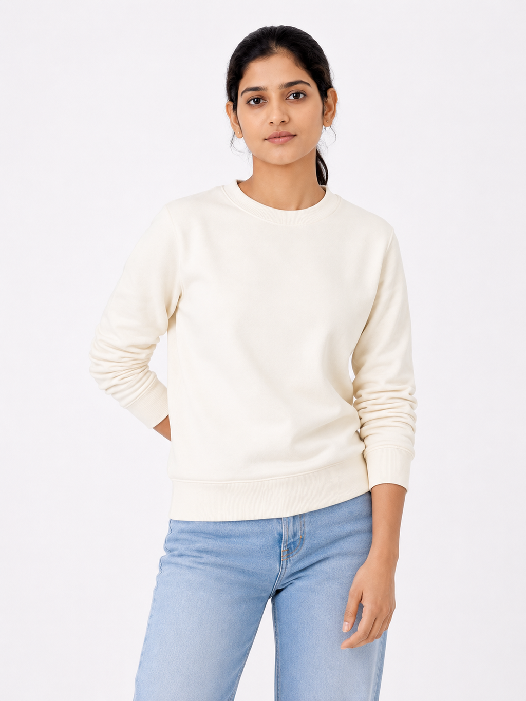 Woman wearing a cream sweater and light blue jeans on a white background