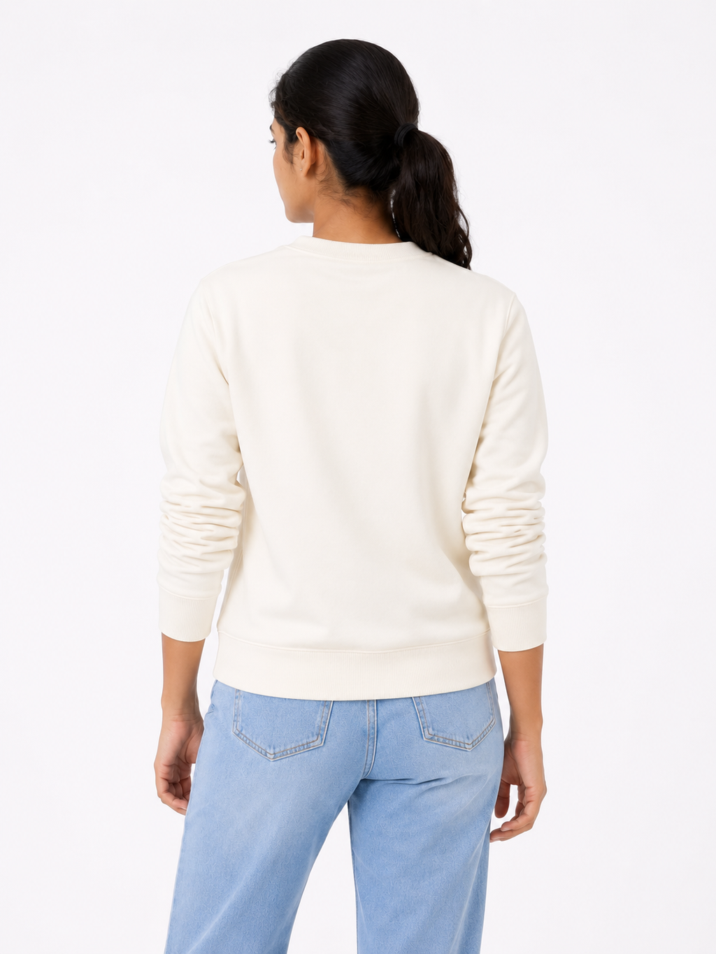 Woman wearing a cream sweater and light blue jeans on a white background