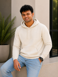 Man wearing a beige hoodie and light blue jeans sitting outdoors.