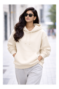 Woman wearing a cream hoodie and sunglasses on a city street