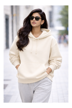 Woman wearing a cream hoodie and sunglasses on a city street