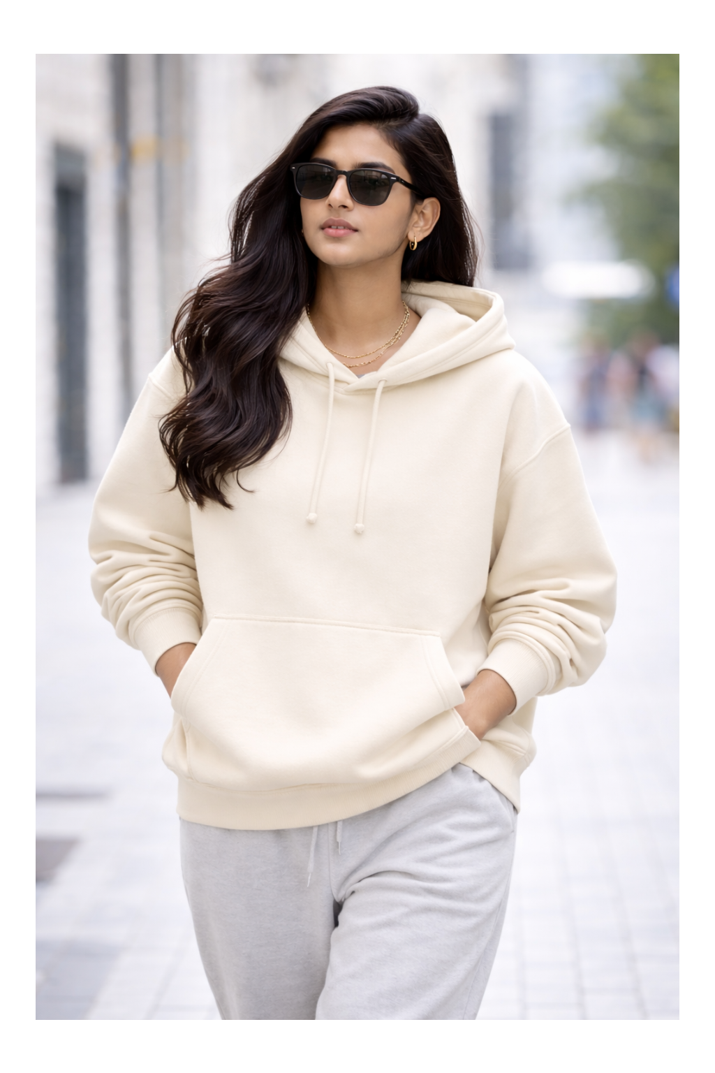 Woman wearing a cream hoodie and sunglasses on a city street