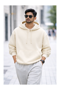 Man wearing a cream hoodie and light gray pants on a city street.