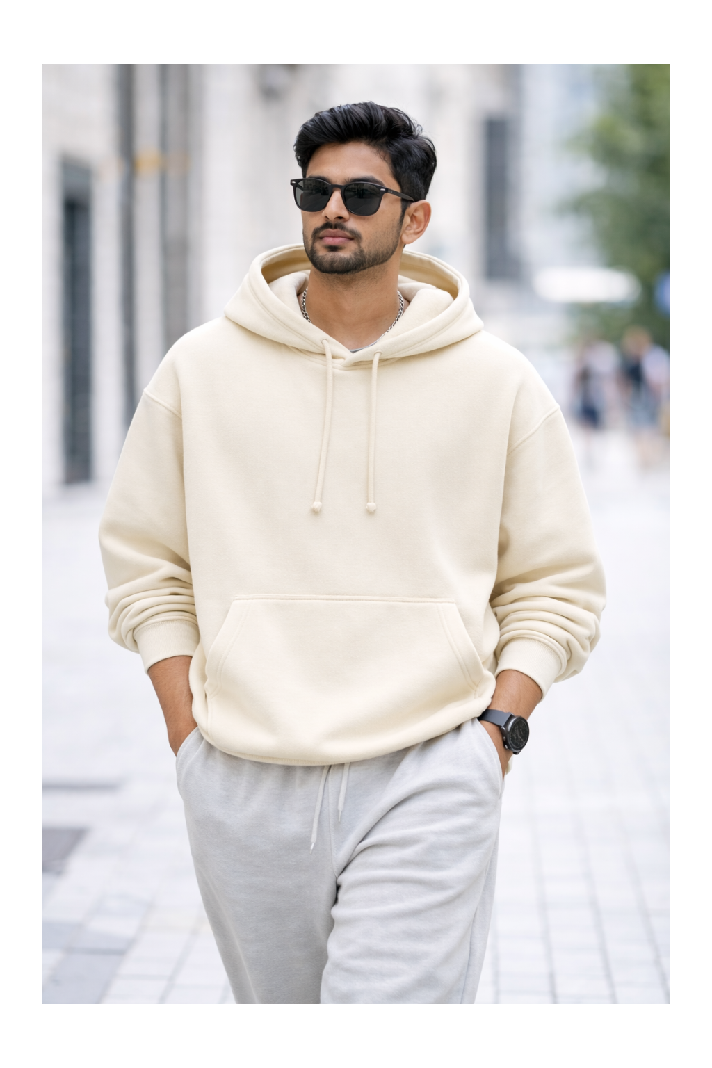 Man wearing a cream hoodie and light gray pants on a city street.