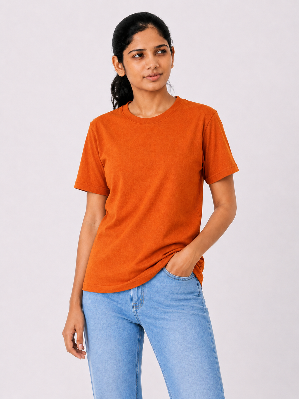 Woman wearing an orange t-shirt and light blue jeans on a plain background