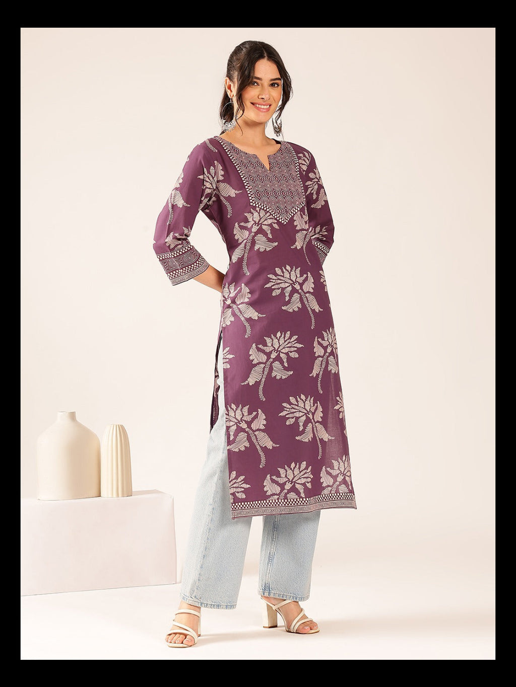 Woman wearing a purple floral patterned kurta with light blue pants on a white background