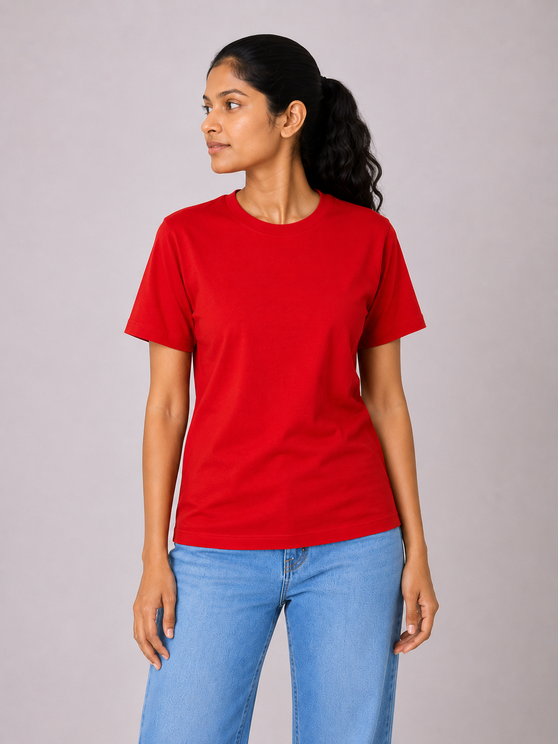 Woman wearing a red t-shirt and blue jeans on a plain background