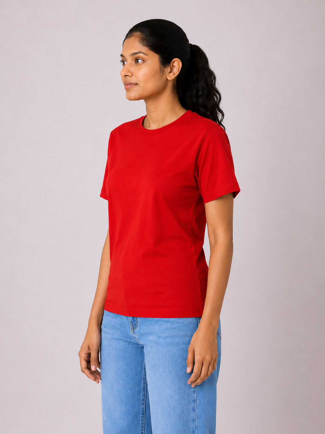 Woman wearing a red t-shirt and blue jeans against a plain background