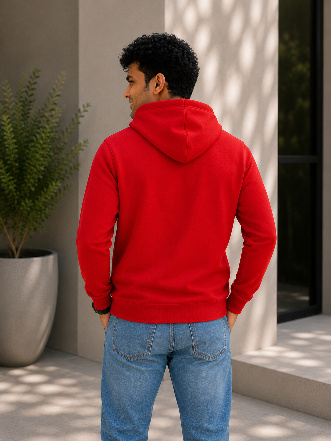 Person wearing a red hoodie and blue jeans standing outdoors.