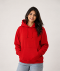 A woman wearing a bright red pullover hoodie with drawstrings and a front kangaroo pocket, paired with light blue jeans, standing against a plain light gray studio background.