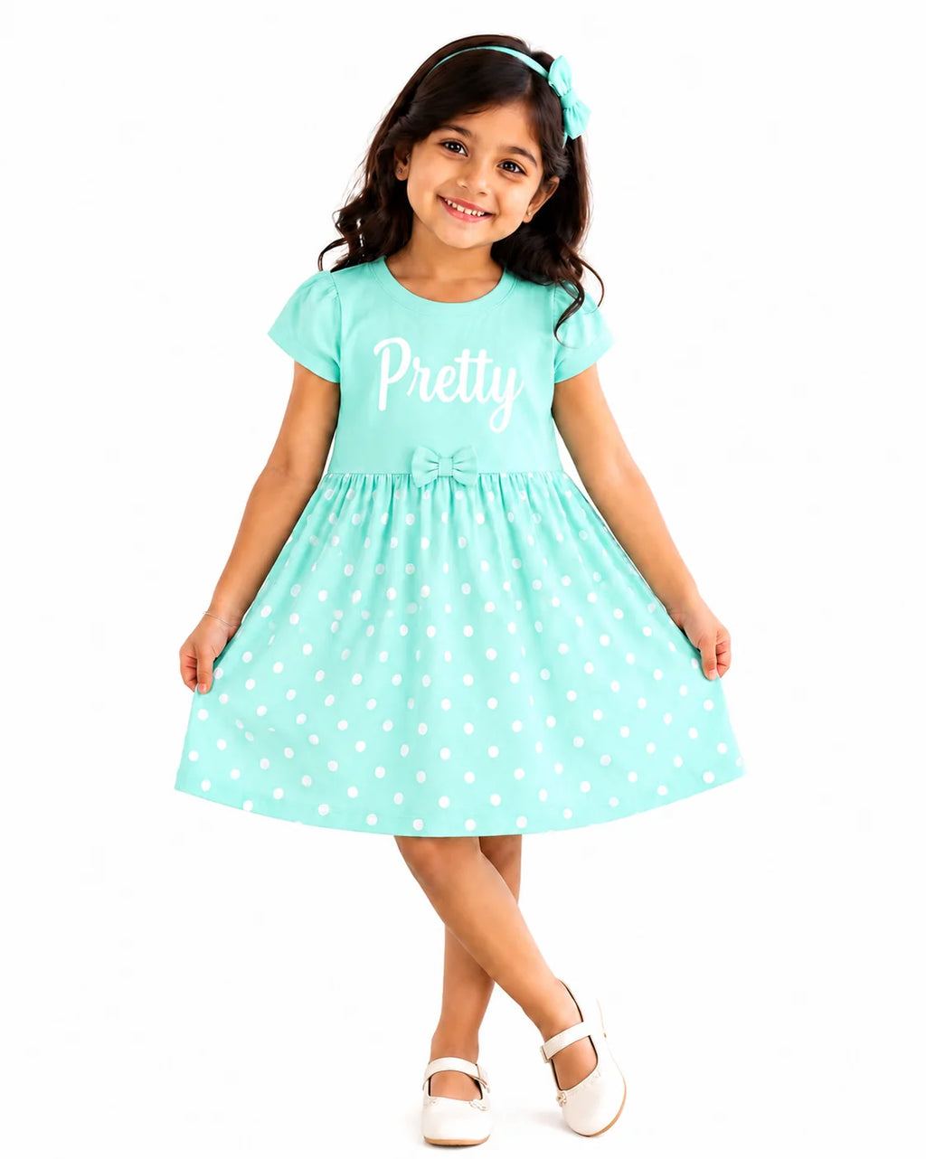A young girl wearing a mint green short-sleeve dress with white polka dots and the word 'Pretty' printed in white on the chest, paired with a matching headband and white shoes, set against a plain white background.